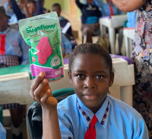 A schoolgirl in uniform holding up a pack of Sussflow reusable pads
